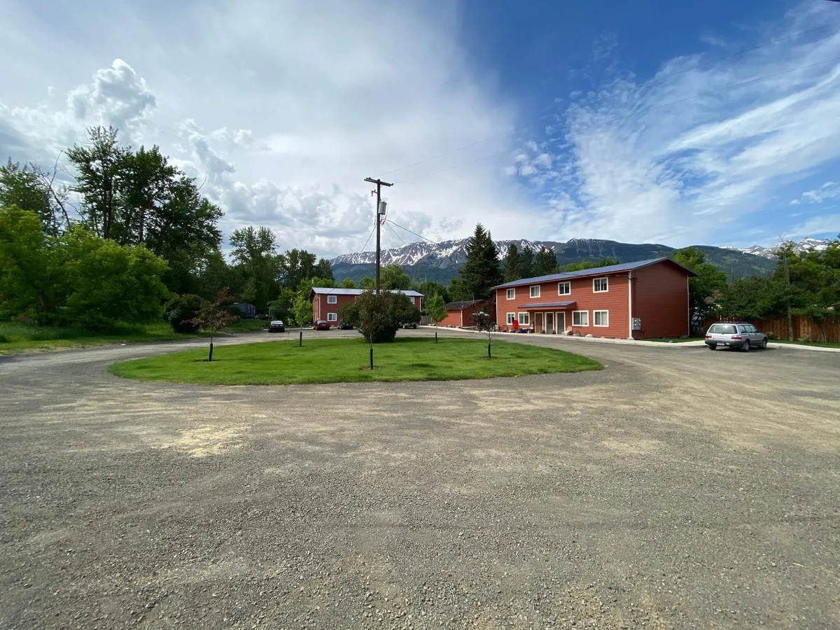 A serene exterior view featuring charming red buildings set on a lush green lawn, with a dramatic mountain backdrop. The inviting outdoor space suggests ample opportunities for family gatherings, nature walks, and casual play, all under the open sky.