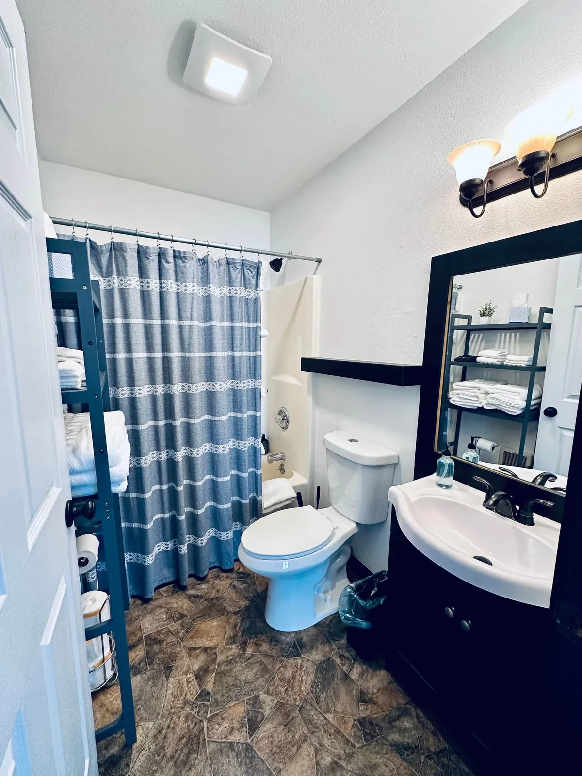 A bright, inviting bathroom featuring a combo tub with a shower curtain drawn partially aside, a sleek vanity with ample countertop space, a towel rack stocked with plush white towels, and a modern toilet. The space is tidy and well-organized, with thoughtful details that promote relaxation and comfort.