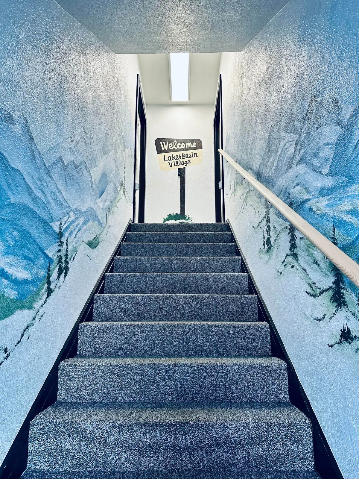 An inviting interior staircase with cheerful murals on the walls and a welcoming sign, suggesting the start of an exploration or the feeling of arrival. The setting feels friendly and accessible for families, encouraging movement and curiosity.