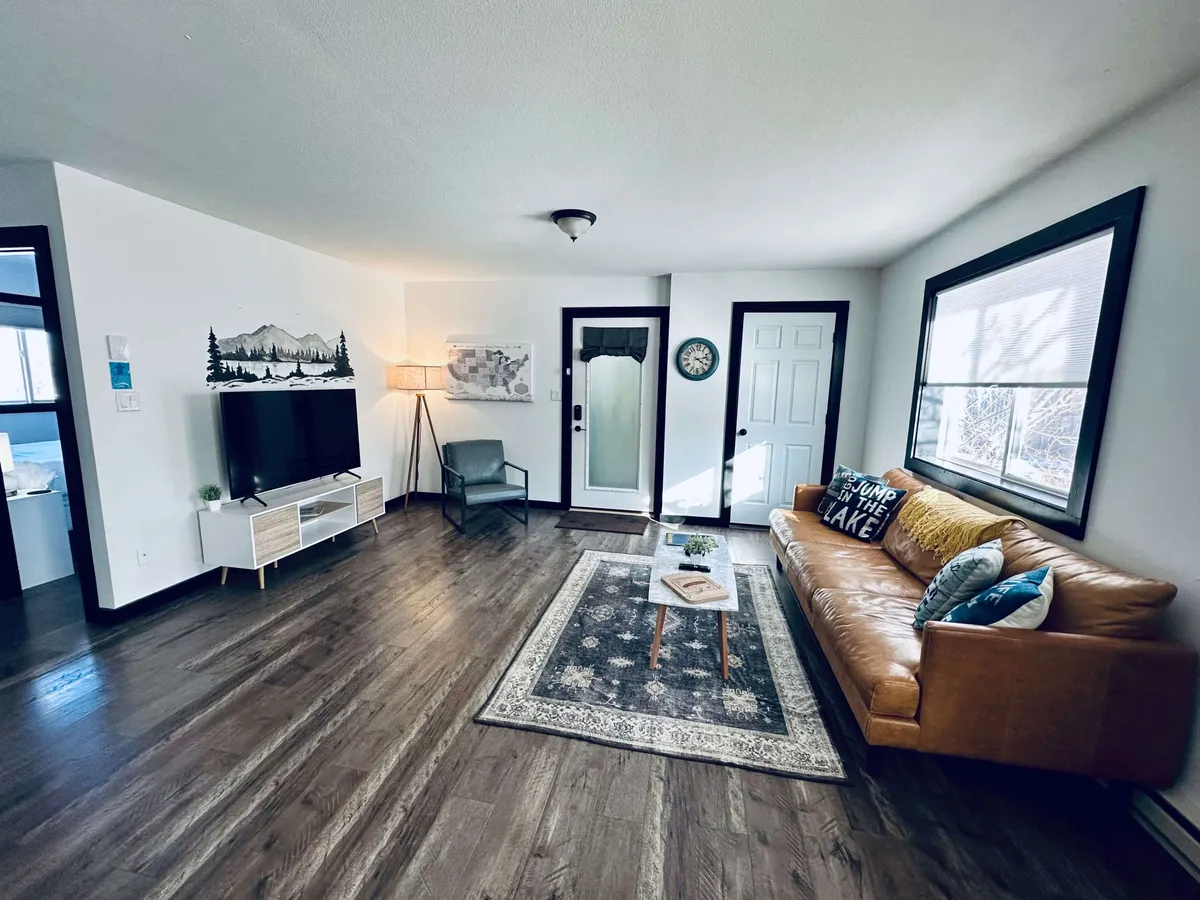 A cozy living room setup with a leather sofa, area rug, TV unit, lamp, and decorative wall art. Ambient lighting and inviting furnishings make the space ideal for unwinding, socializing, or enjoying a quiet moment with a book or coffee.